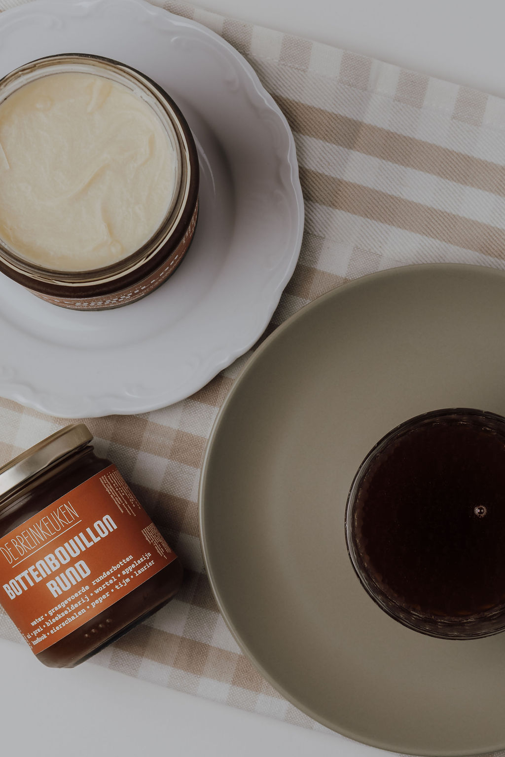 Open pot zuurkool met een pitje, een kom bottenbouillon en een pot runderbottenbouillon van De Breinkeuken op een geruite doek