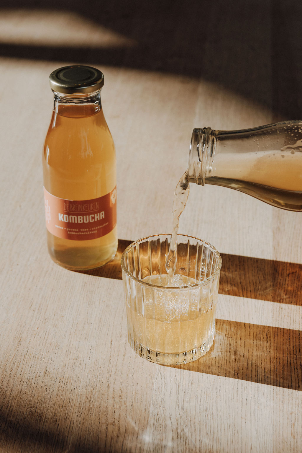 Fles kombucha van De Breinkeuken wordt ingeschonken in een glas